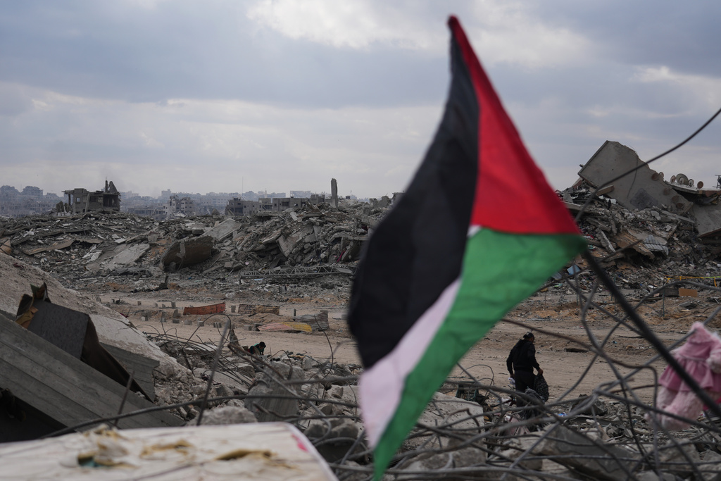 A displaced man walks past a Palestinian flag placed over the rubble of destroyed buildings in Gaza City, Sunday, Oct. 12, 2025, after Israel and Hamas agreed to a temporary pause in their war and the release of the remaining hostages. (AP Photo/Abdel Kareem Hana)