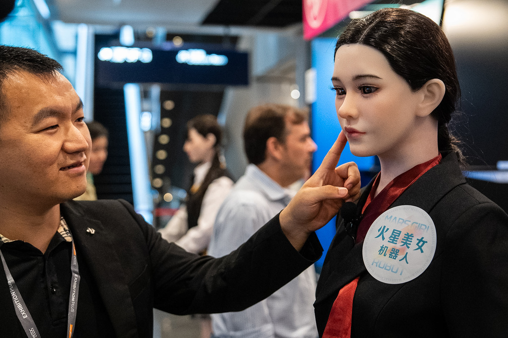 A member of staff touches the face of a humanoid robot showcased at an exhibition in Hong Kong on Monday, April 13, 2026. (AP Photo/ Chan Long Hei)
