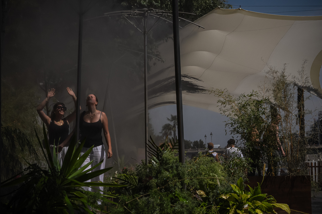 Two women cool off under misting sprayers in Paris during a heat wave, Saturday, July 11, 2026. (AP Photo/Aurelien Morissard)