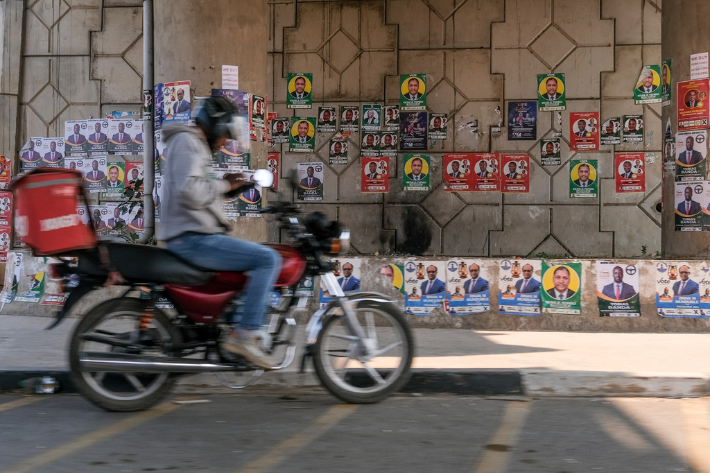 A motor bike delivery rider waits next a wall covered with electoral campaign posters in Lusaka, Zambia, Saturday, Aug. 8, 2026. (AP Photo/Anita Reed)