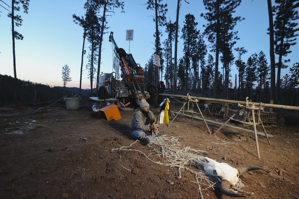 A demonstrator sits cross legged in front of drilling equipment near Pe'Sla on Thursday morning, April 30, 2026, in Pennington County, S.D. (Angel White Eyes via AP)