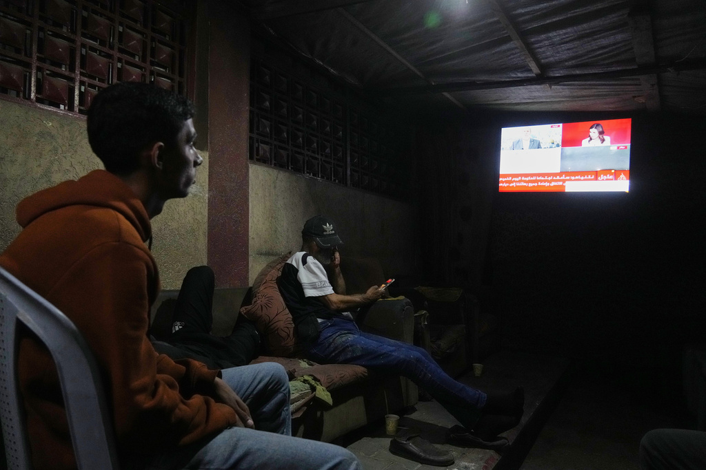 Palestinians follow the news on a television after the announcement that Israel and Hamas have agreed to the first phase of a peace plan to pause fighting, as they sit in a tent outside Al-Aqsa Hospital, in Deir al-Balah, in the central Gaza Strip, Thursday, Oct. 9, 2025. (AP Photo/Abdel Kareem Hana)
