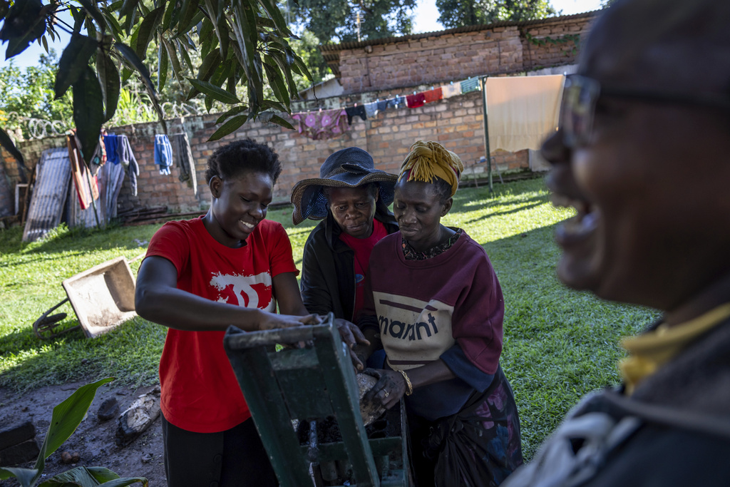 Whitney Catherine Among, 20, from left, learns how to make charcoal briquettes from Christine Nalumu, 64, and Saniya Nakimuli, 65, part of a program by the NGO Health Nest Uganda, Monday, Nov. 25, 2024, in Entebbe, Uganda. The program helps both groups to share their skills with one another, from teaching youths how to make briquettes used for cooking and heating and seniors learning about technology from the younger generation. (AP Photo/David Goldman)