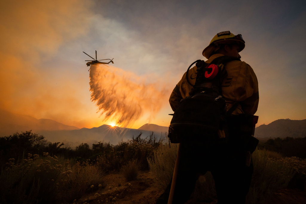 FILE - A firefighter watches as a helicopter drops water on the Summit Fire while battling wildfires in Llano, Calif., July 10, 2026. (AP Photo/Ethan Swope, File)
