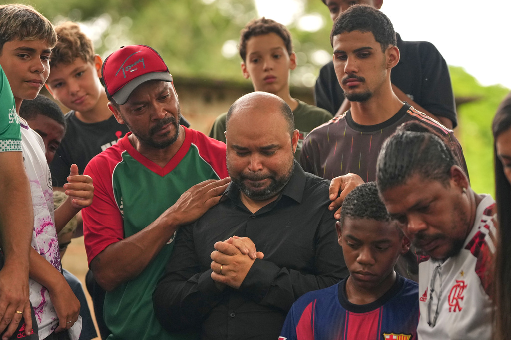Ricardo Dutra, center, the father of 11-year-old Bernardo Lopes, a victim of heavy rains and flooding, is comforted by his son's friends during the burial of his child in Juiz de Fora, Minas Gerais state, Brazil Wednesday, Feb. 25, 2026. (AP Photo/Silvia Izquierdo)