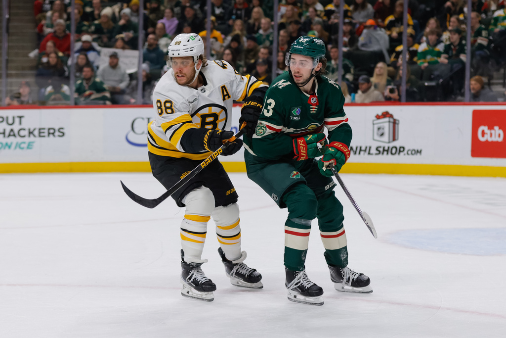 Minnesota Wild defenseman Quinn Hughes, right, and Boston Bruins right wing David Pastrnak (88) battle for position during the first period of an NHL hockey game, Sunday, Dec. 14, 2025, in St. Paul, Minn. (AP Photo/Bailey Hillesheim)