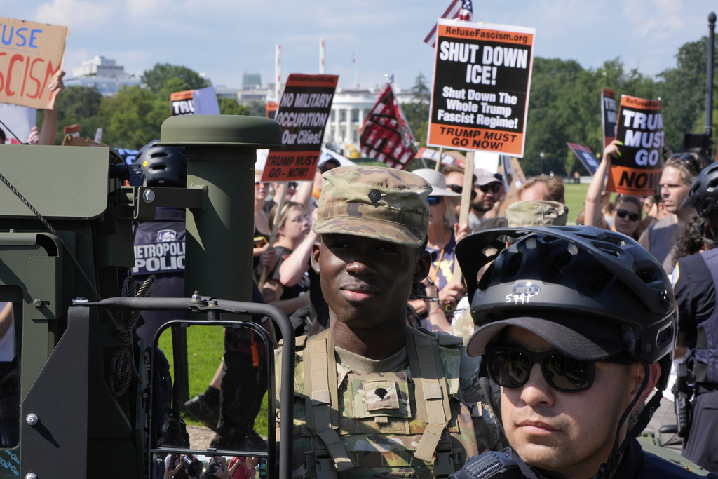 Washington Metropolitan Police officers and military police soldiers with the District of Columbia National Guard watch as activists protest President Donald Trump's federal takeover of policing of the District of Columbia, Saturday, Aug. 16, 2025, in Washington. (AP Photo/Alex Brandon)