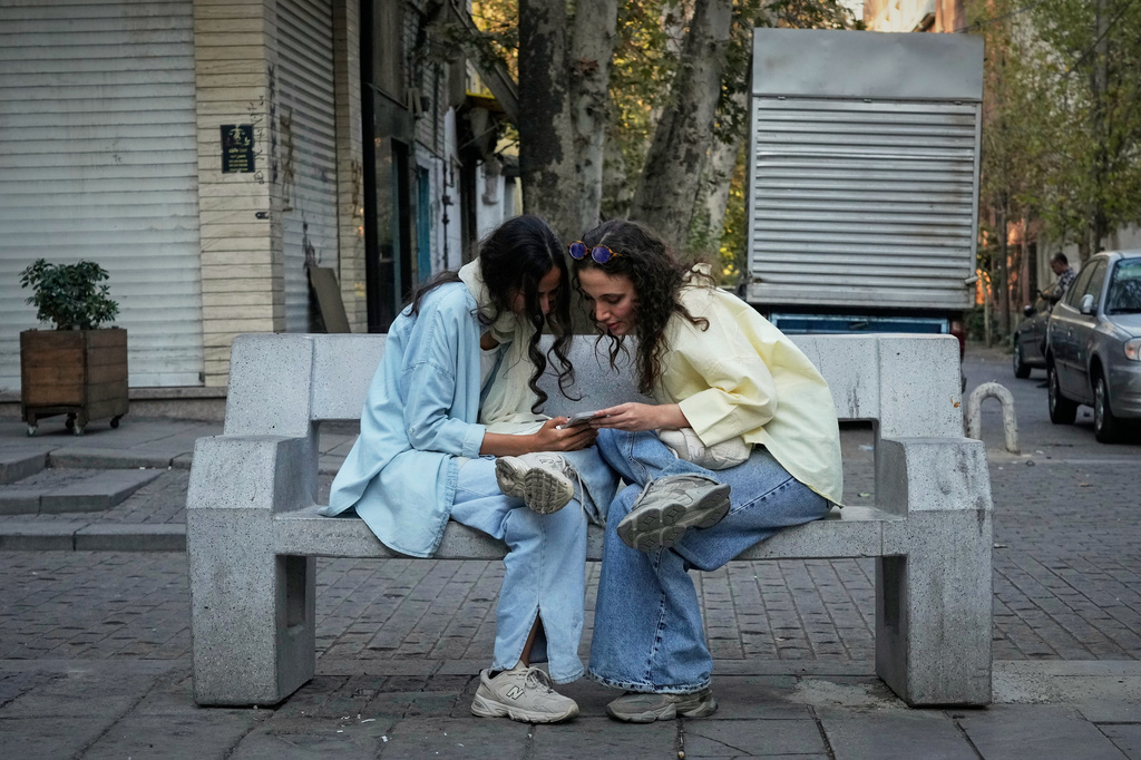 FILE - Two women use a smartphone in northern Tehran, Iran, Sept. 28, 2025. (AP Photo/Vahid Salemi, File)