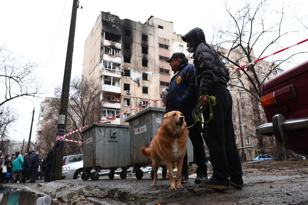 Local residents walk a dog near a damaged apartment building hit by Russian drone in Zaporizhzhia, Ukraine, Thursday, Feb. 26, 2026. (AP Photo/Kateryna Klochko)