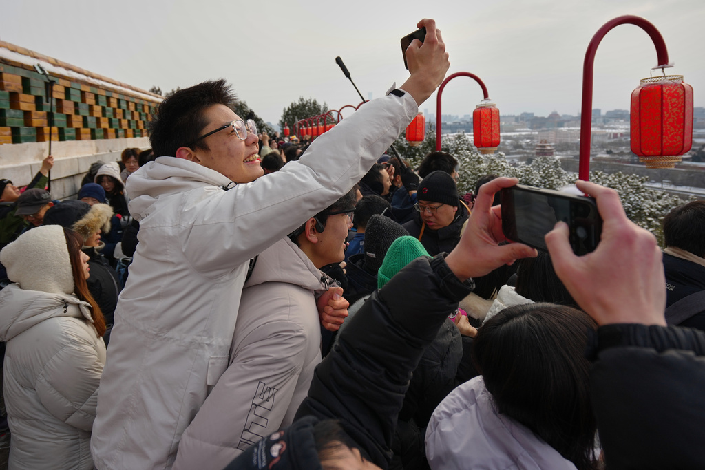 People catch a sight of the snow-covered Forbidden City from a pavilion with lantern decorations at the Jingshan Park a day after the snow fall, in Beijing, Sunday, Jan. 18, 2026. (AP Photo/Andy Wong)
