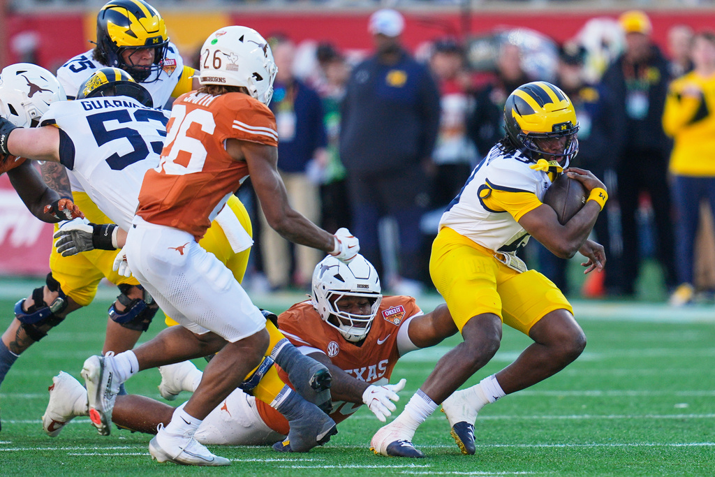 Michigan quarterback Bryce Underwood, right, scrambles for yardage as he gets past Texas defensive lineman Lavon Johnson, center, and linebacker Ty'Anthony Smith (26) during the first half of the Citrus Bowl NCAA college football game, Wednesday, Dec. 31, 2025, in Orlando, Fla. (AP Photo/John Raoux)