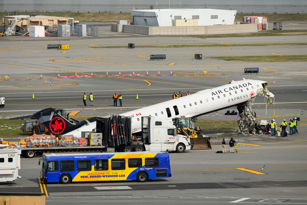 Officials inspect the wreckage of an Air Canada Express jet, Wednesday, March 25, 2026, just off the runway where it had collided with a Port Authority fire truck Sunday night at LaGuardia Airport in New York. (AP Photo/Yuki Iwamura)