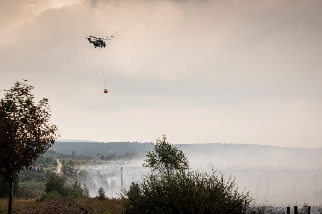 A helicopter prepares to dump a Bambi Bucket of water over a field as a wildfire burns near Waimes, Belgium, Monday, Aug. 17, 2026. (AP Photo/Valentin Bianchi)