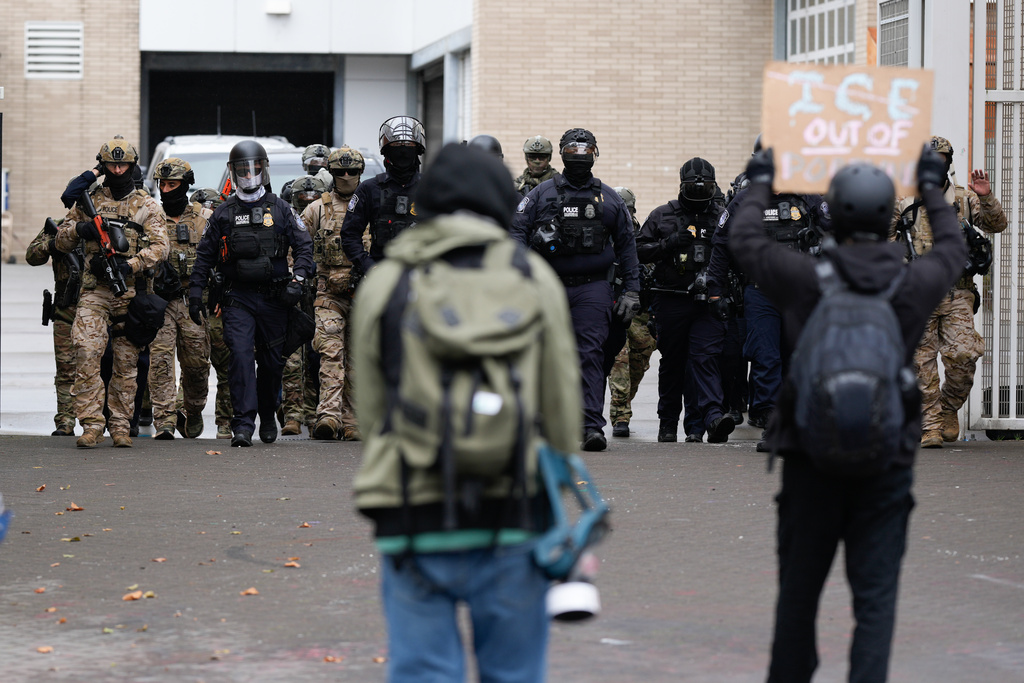 People protest outside a U.S. Immigration and Customs Enforcement facility as law enforcement officers walk out of the gates to guard vehicles leaving the facility on Saturday, Oct. 11, 2025, in Portland, Ore. (AP Photo/Jenny Kane)