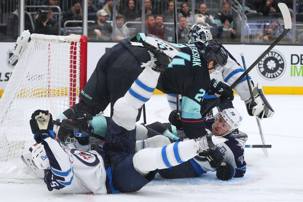 Seattle Kraken defenseman Jamie Oleksiak (24) falls over Winnipeg Jets left wing Tanner Pearson (70) during a pile-up at the net during the third period of an NHL hockey game Thursday, Nov. 13, 2025, in Seattle. (AP Photo/Lindsey Wasson)