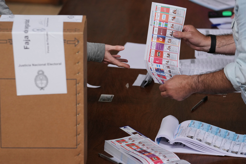 An electoral official handles a ballot to a voter during legislative midterm elections, in La Plata, Argentina, Sunday, Oct. 26, 2025. (AP Photo/Gustavo Garello)