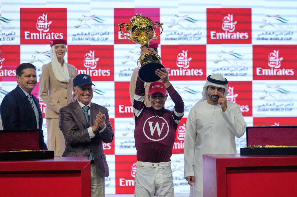 Jockey Jose Ortiz, second right, holds the trophy after riding Magnitude to win the $12 million Dubai World Cup over 2000m (10 furlongs) at Meydan Racecourse in Dubai, the United Arab Emirates, Saturday, March 28, 2026. At left is owner Ron Winchell, and assistant trainer Scott Blasi. (AP Photo/Altaf Qadri)