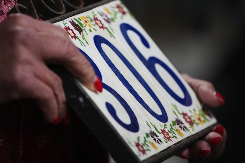 Jill Genzon holds a placard with her home address, which she lost in the Eaton Fire, on the one-year anniversary of the fire Wednesday, Jan. 7, 2026, in Altadena, Calif. (AP Photo/Gregory Bull)