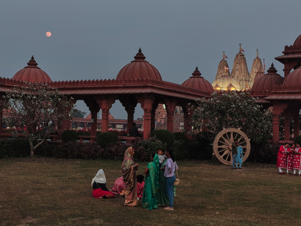 Devotees relax in the garden as a supermoon, the last full moon of the year, rises up on the sky over the Swaminarayan Temple, in Kolkata, India, Thursday, Dec. 4, 2025. (AP Photo/Bikas Das)