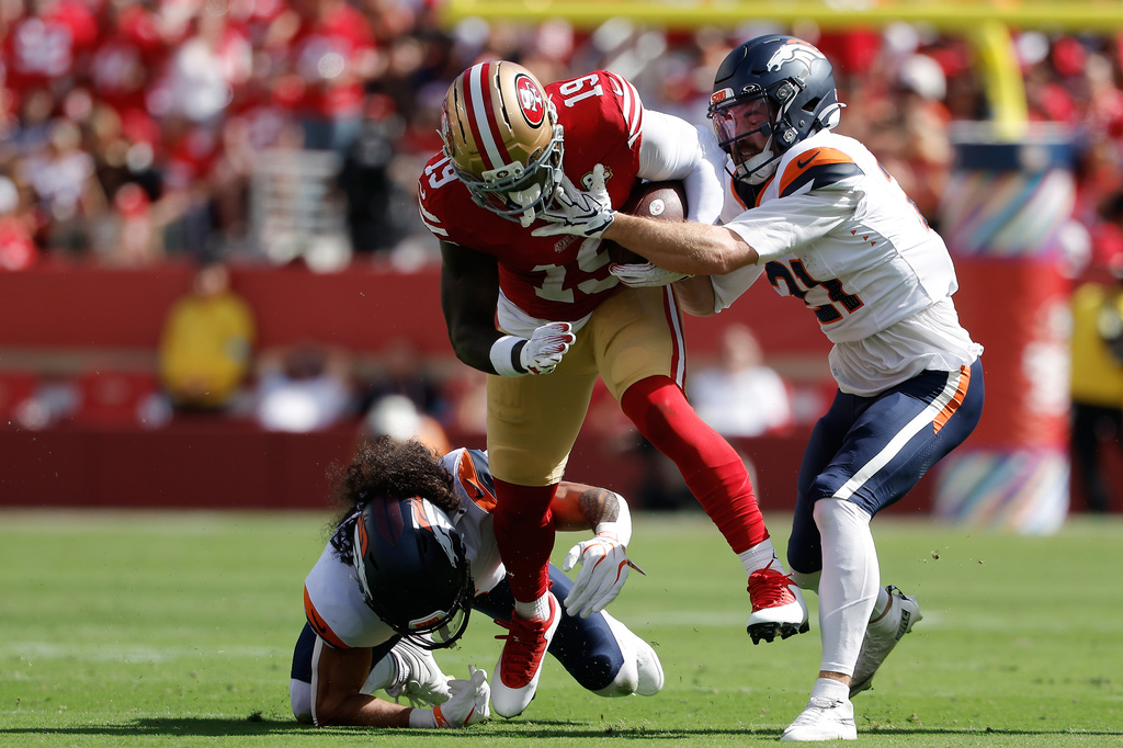 San Francisco 49ers wide receiver Deebo Samuel Sr., middle, runs against Denver Broncos safety Talanoa Hufanga, bottom, and cornerback Riley Moss (21) during the first half of an NFL football game in Santa Clara, Calif., Sunday, Oct. 4, 2026. (AP Photo/Kelley L. Cox)