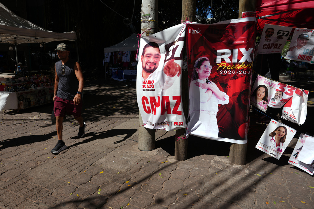 A man walks past a stand with campaign posters of ruling party presidential candidate Rixi Moncada in Tegucigalpa, Honduras, Thursday, Nov. 27, 2025 prior to general elections. (AP Photo/Moises Castillo)