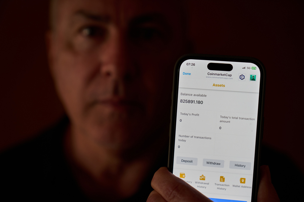 Chris Colocousis holds up a screenshot of the fake app where he invested his savings showing his account had more than doubled to nearly $826,000 as part of a scam in which he says he lost $400,000 at his home in Raynham, Mass., Tuesday, March 10, 2026. (AP Photo/David Goldman)