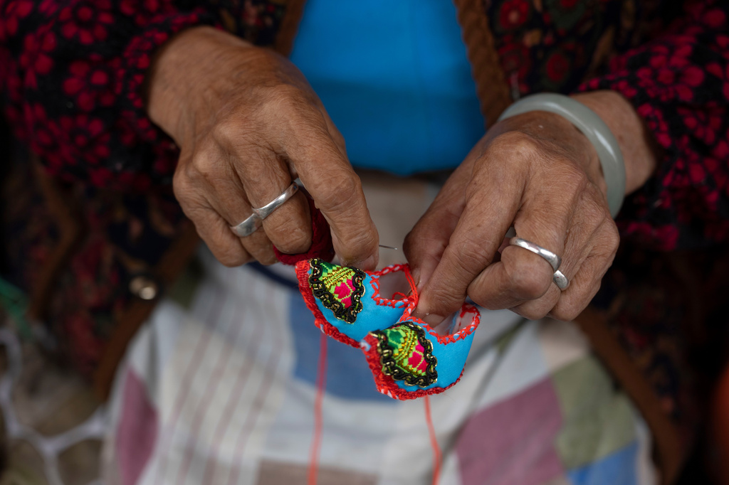 An elderly woman knits miniature shoes to sell to tourists at Tianlong Tunpu, an ancient town in southwestern China's Guizhou province on Thursday, May 28, 2026. (AP Photo/Ng Han Guan)
