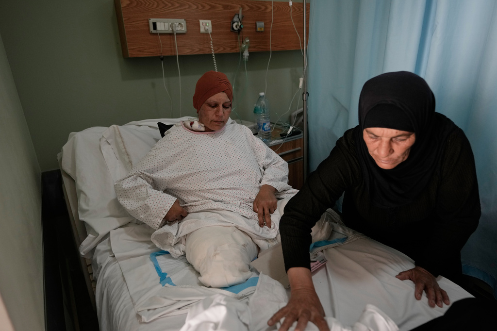 Sanaa Khalil, 35, a Syrian farmer who lost her two legs in the past days by an Israeli airstrike while she was working at a banana plantation, lies on a bed as she is assisted by a relative at a hospital in the southern port city of Tyre, Lebanon, Friday, May 1, 2026. (AP Photo/Hussein Malla)