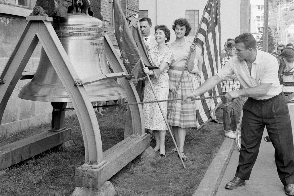 FILE - Romer Derr rings a replica of the Liberty Bell outside the Federal Building 49 times, signifying Alaska's joining the United States as the 49th state, on July 1, 1958, in Juneau, Alaska. Behind Derr holding the Alaska flag, left, is Judy Findlay and holding the U.S. flag, right, is Marilee Nowacki. (AP Photo/JK, File)