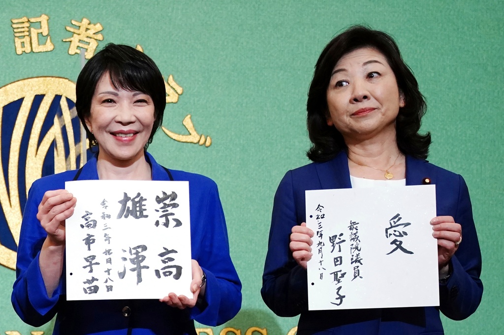 FILE - Sanae Takaichi, left, and Seiko Noda, right, both former internal affairs ministers and candidates for the presidential election of the ruling Liberal Democratic Party, show their motto on cards, during a debate session held by the Japan National Press Club, Sept. 18, 2021, in Tokyo. (AP Photo/Eugene Hoshiko, Pool, File)