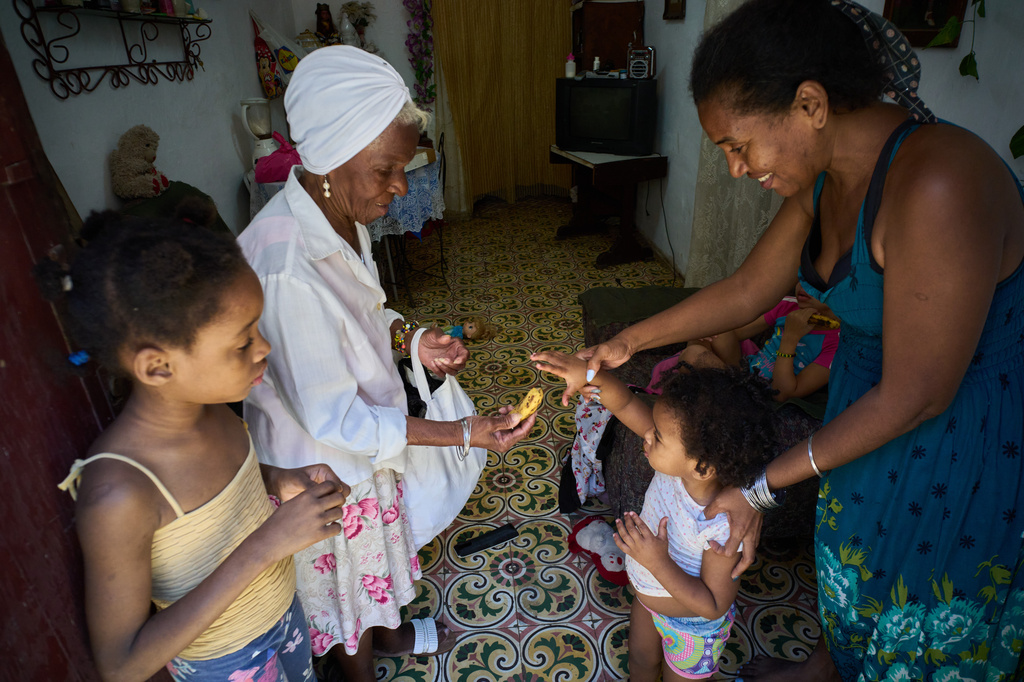 Yuneisy Riviaux helps her daughter Seinet to reach for a banana from a friend at their home in Havana, Cuba, Wednesday, March 25, 2026. (AP Photo/Ramon Espinosa)