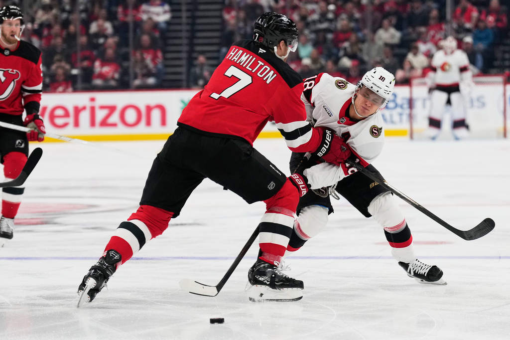 Ottawa Senators' Tim St&uuml;tzle, right, tries to pass around New Jersey Devils' Dougie Hamilton during the first period of an NHL hockey game in Newark, N.J., Monday, Oct. 12, 2026. (AP Photo/Seth Wenig)