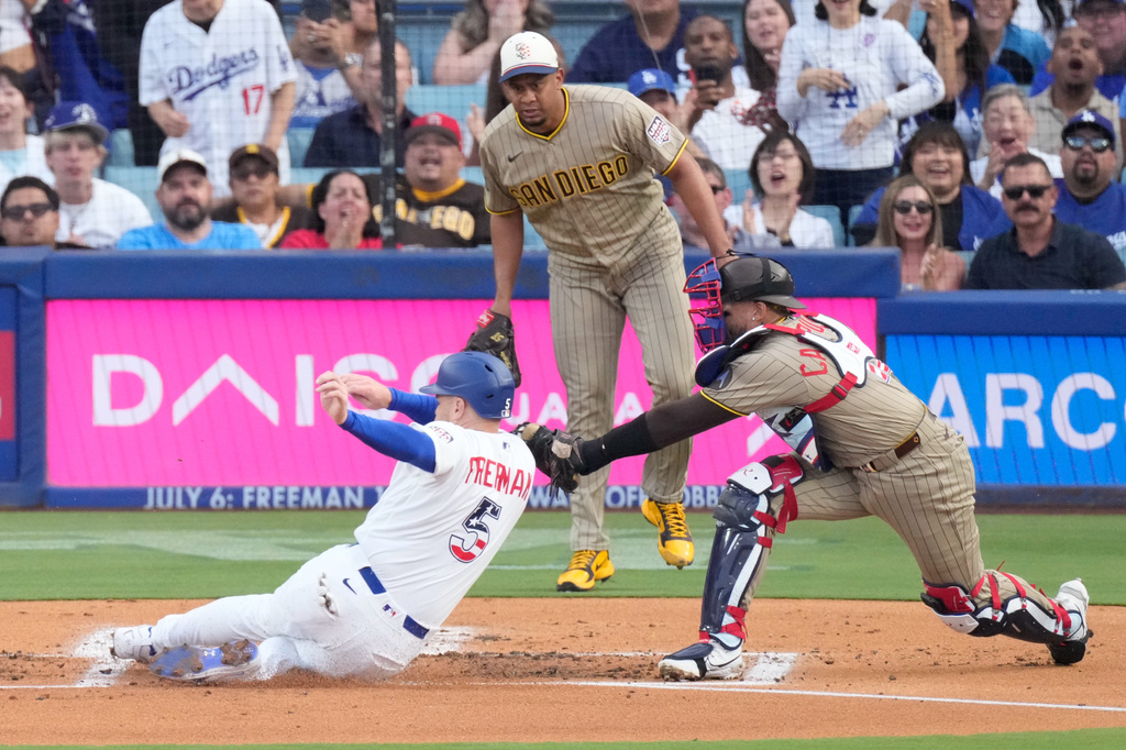 Los Angeles Dodgers' Freddie Freeman, left, is tagged out by San Diego Padres catcher Luis Campusano, right, as he tries to score on a double by Mookie Betts while starting pitcher Wandy Peralta watches during the first inning of a baseball game Saturday, July 4, 2026, in Los Angeles. (AP Photo/Mark J. Terrill)