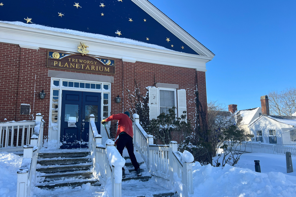 A worker shovels snow from the steps of the Treworgy Planetarium at the Mystic Seaport Museum in Mystic, Conn., Tuesday, Feb. 24, 2026, following a snowstorm. (Shannon McKenzie/Mystic Seaport Museum via AP)