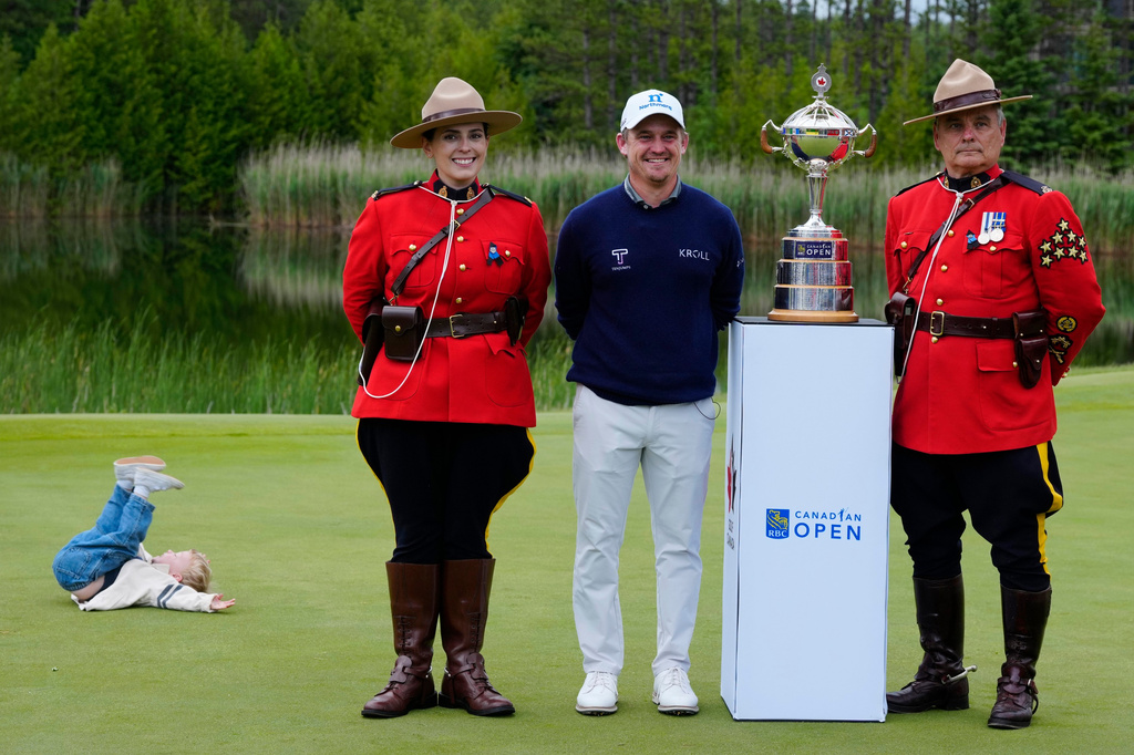 A child, left, of Bud Cauley, second from right, plays as Bud stands with two RCMP officers next to the trophy after he won the Canadian Open golf tournament in Caledon, Ontario, Sunday June 14, 2026. (Frank Gunn/The Canadian Press via AP)