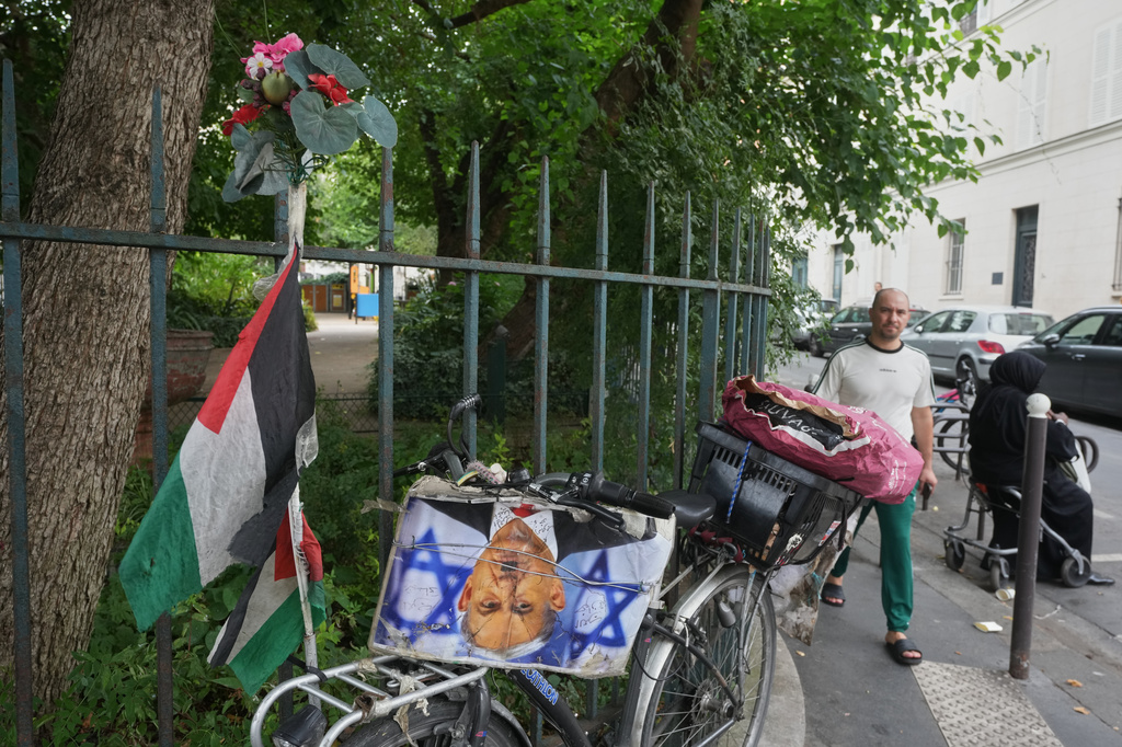 A man walks past a bicycle displaying a Palestinian flag and a photograph depicting Israeli Prime Minister Benjamin Netanyahu as Nazi dictator Adolf Hitler outside the Grand Mosque of Paris as it celebrates its 100th anniversary, Friday, July 17, 2026. (AP Photo/Michel Euler)