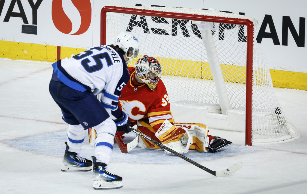 Winnipeg Jets' Mark Scheifele, left, scores on Calgary Flames goalie Dustin Wolf during third period NHL hockey action in Calgary, Alta., Monday, Oct. 20, 2025. (Jeff McIntosh/The Canadian Press via AP)