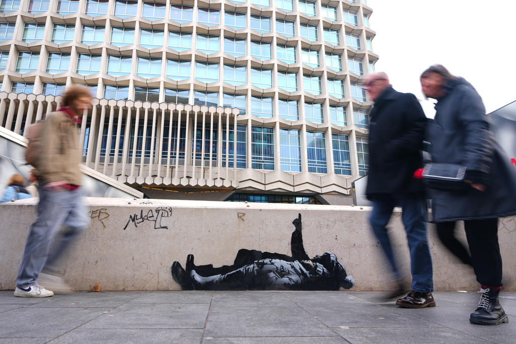 Pedestrians walk past a graffiti artwork, depicting two people, outside Tottenham Court Road Station in London, Monday, Dec. 22, 2025 as elusive street artist Banksy appeared to confirm Monday that an identical image appeared on a wall on the side of a building in Bayswater, west London is his latest work. (AP Photo/Kirsty Wigglesworth)
