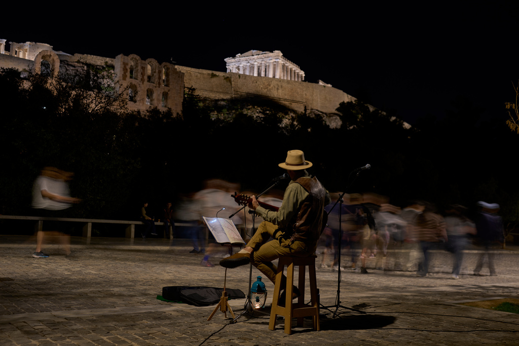 Street musician Marinos Kyriakopoulos performs as pedestrians walk by in front of the Parthenon temple atop the Acropolis hill, in Athens, Tuesday Oct. 28, 2025. (AP Photo/Petros Giannakouris)