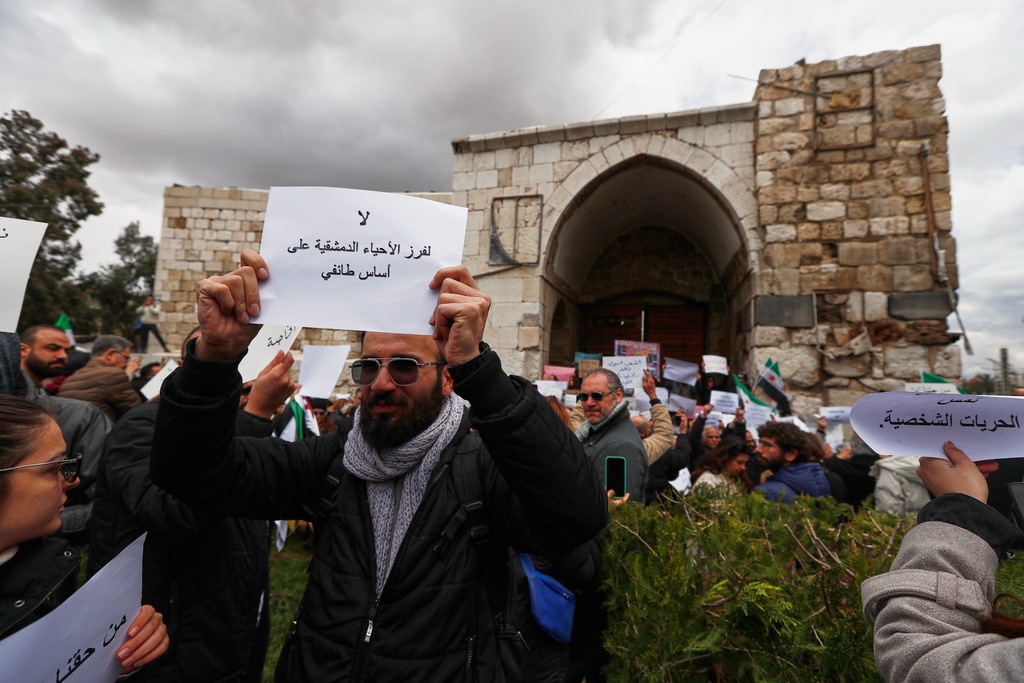 A man holds a sign reading in Arabic, "No to dividing Damascus neighborhoods along sectarian lines," during a demonstration against new restrictions limiting alcohol sales mainly to Christian neighborhoods in Damascus, Syria, Sunday, March 22, 2026. (AP Photo/Omar Sanadiki)