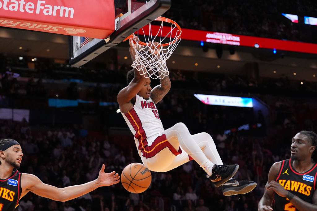 Miami Heat forward Myron Gardner swings on the basket after dunking over Atlanta Hawks forward Asa Newell, left, and guard Keaton Wallace, during the second half of an NBA basketball game, Sunday, April 12, 2026, in Miami. (AP Photo/Rebecca Blackwell)
