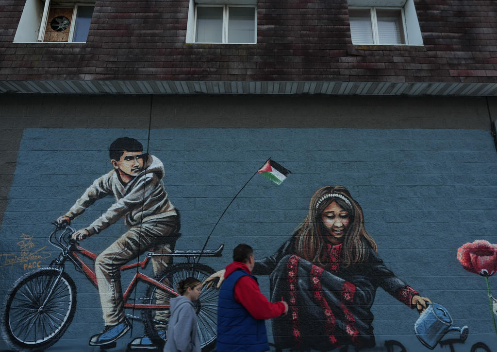 Passersby walk in front of a mural in "Palestine Way," a section of Main Street in the South Paterson neighborhood of Paterson, N.J. during Ramadan on Friday, Feb. 27, 2026. (AP Photo/Luis Andres Henao)