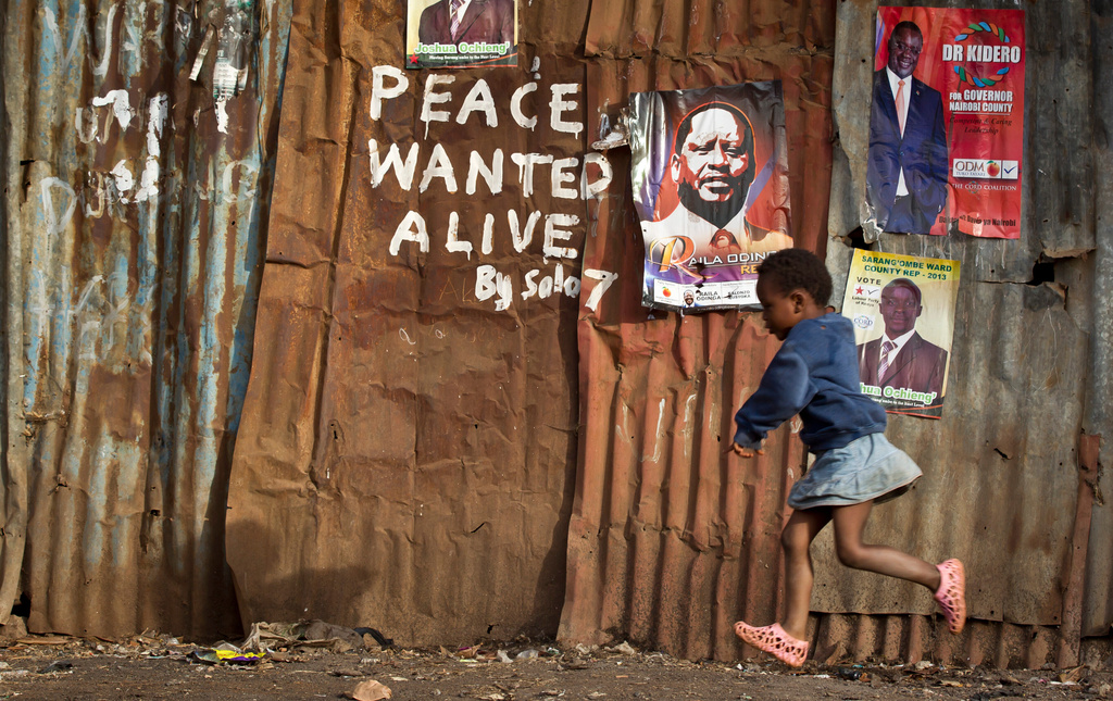 A young girl runs past pro-peace graffiti written during the post-election violence of the previous election in 2007 and a poster of presidential candidate Raila Odinga, center-right, in the Kibera slum of Nairobi, Kenya Wednesday, March 6, 2013. (AP Photo/Ben Curtis)