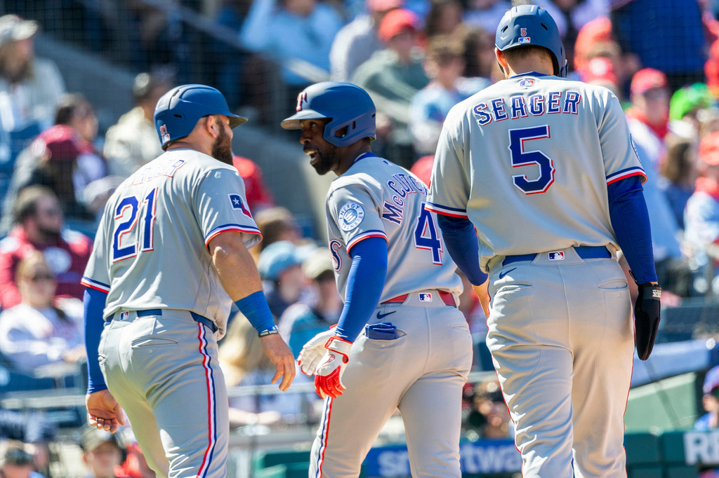 Texas Rangers' Andrew McCutchen, center, celebrates his three run home run with Jake Burger (21) Corey Seager (5) in the fourth inning of a baseball game against the Philadelphia Phillies, Sunday, March 29, 2026, in Philadelphia. (AP Photo/Laurence Kesterson)