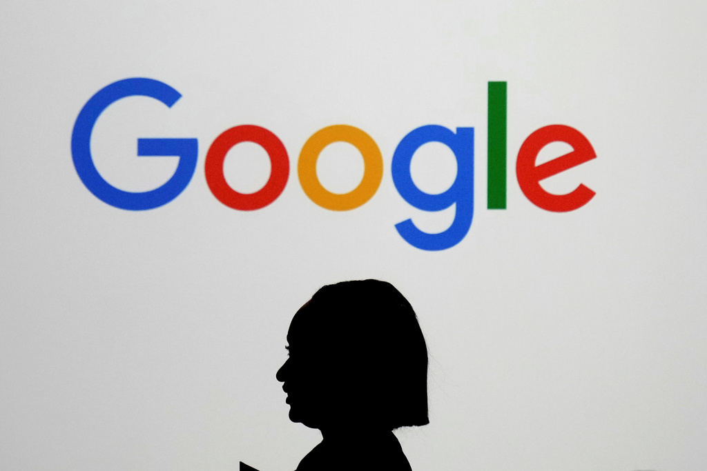FILE - A woman walks by a giant screen with a logo at an event at the Paris Google Lab on the sidelines of the AI Action Summit in Paris, on Feb. 9, 2025. (AP Photo/Thibault Camus,File)