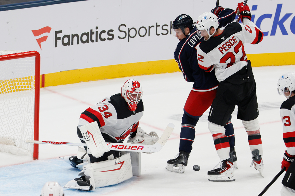 New Jersey Devils' Jake Allen, left, makes a save as teammate Brett Pesce, top right, and Columbus Blue Jackets' Charlie Coyle, second from left, fight for position during the second period of an NHL hockey game, Monday, Oct. 13, 2025, in Columbus, Ohio. (AP Photo/Jay LaPrete)