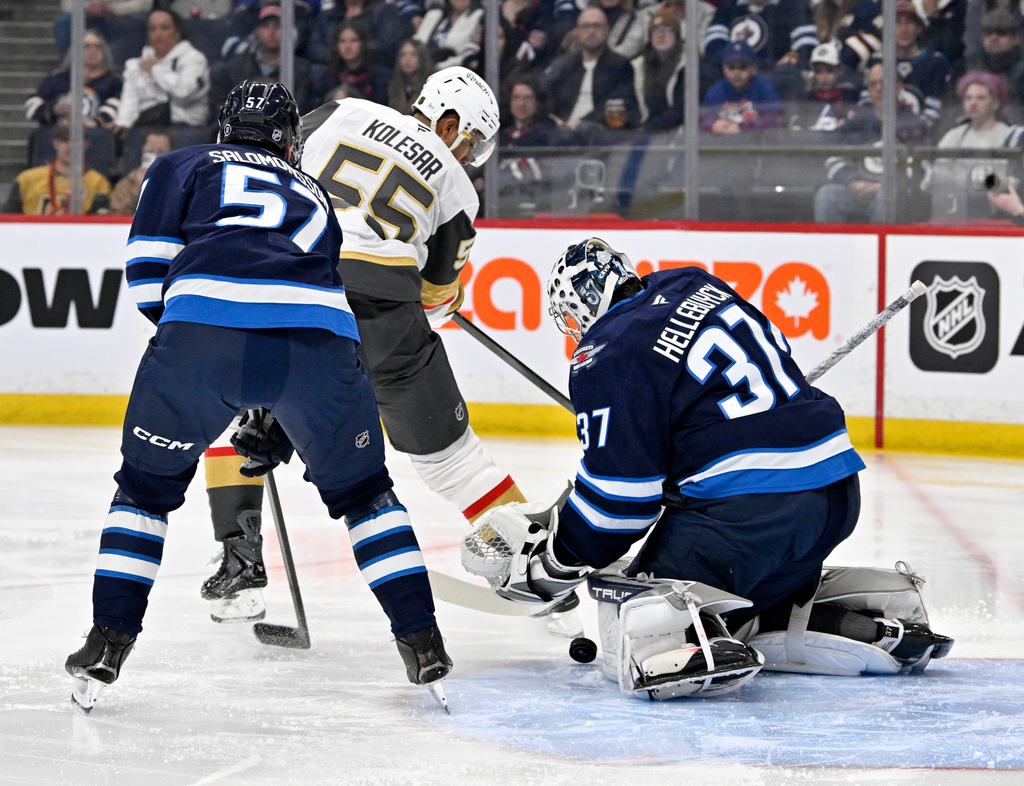 Winnipeg Jets goaltender Connor Hellebuyck (37) makes a save on Vegas Golden Knights' Keegan Kolesar (55) as Elias Salomonsson (57) defends during the first period of their NHL hockey game in Winnipeg, Tuesday March 24, 2026. (Fred Greenslade/The Canadian Press via AP)