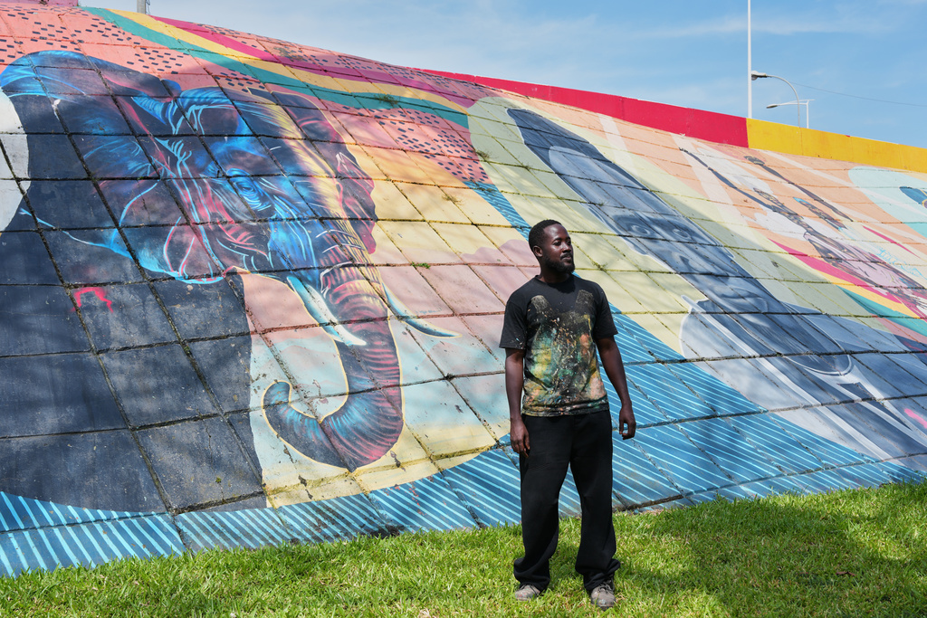 Graffiti artist Omar Diaw stands In front of one of his murals in Conakry, Guinea, Saturday, Sep. 20, 2025. (AP Photo/Misper Apawu)