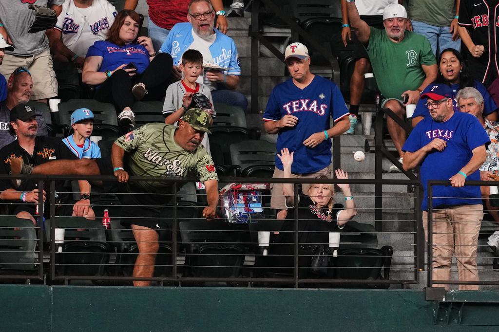 A fan attempts to reach a three-run home run ball hit by Boston Red Sox's Trevor Story in the eighth inning of a baseball game against the Texas Rangers Thursday, Sept. 17, 2026, in Arlington, Texas (AP Photo/Tony Gutierrez)