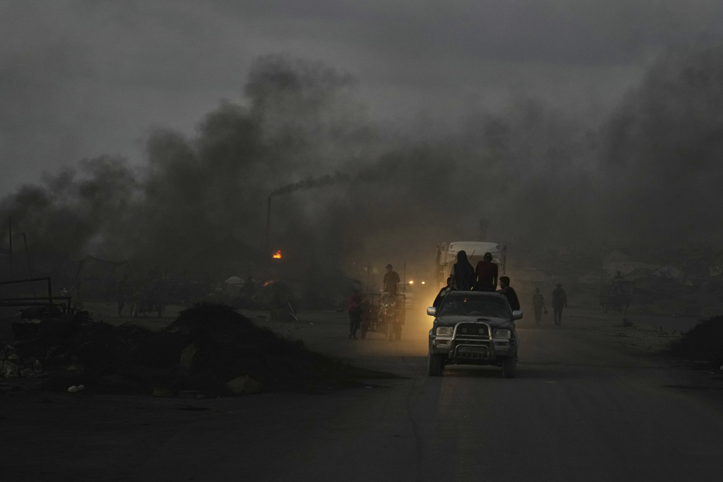 Palestinians ride their vehicles through black smoke from makeshift burners used to extract fuel from melted plastic along the Sea Road, at dusk in the south of Gaza City, Thursday, Aug. 21, 2025. (AP Photo/Abdel Kareem Hana)